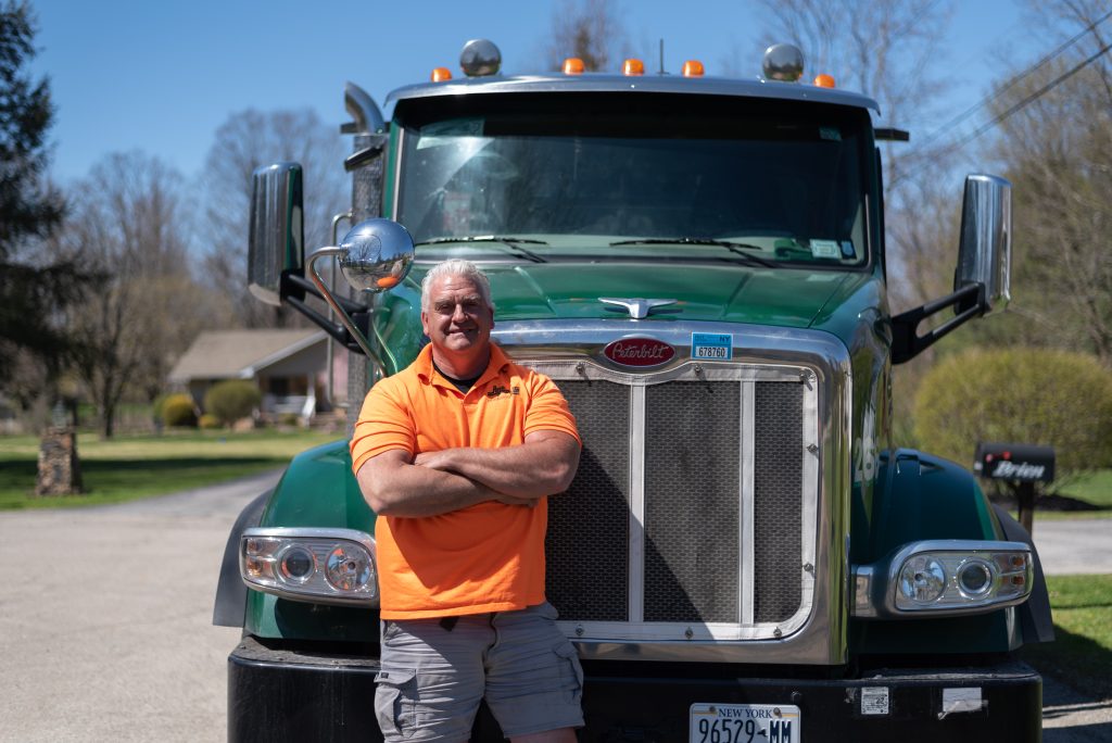 Royal Carting Employee wearing an orange shirt standing with arms crossed in front of a green garbage truck
