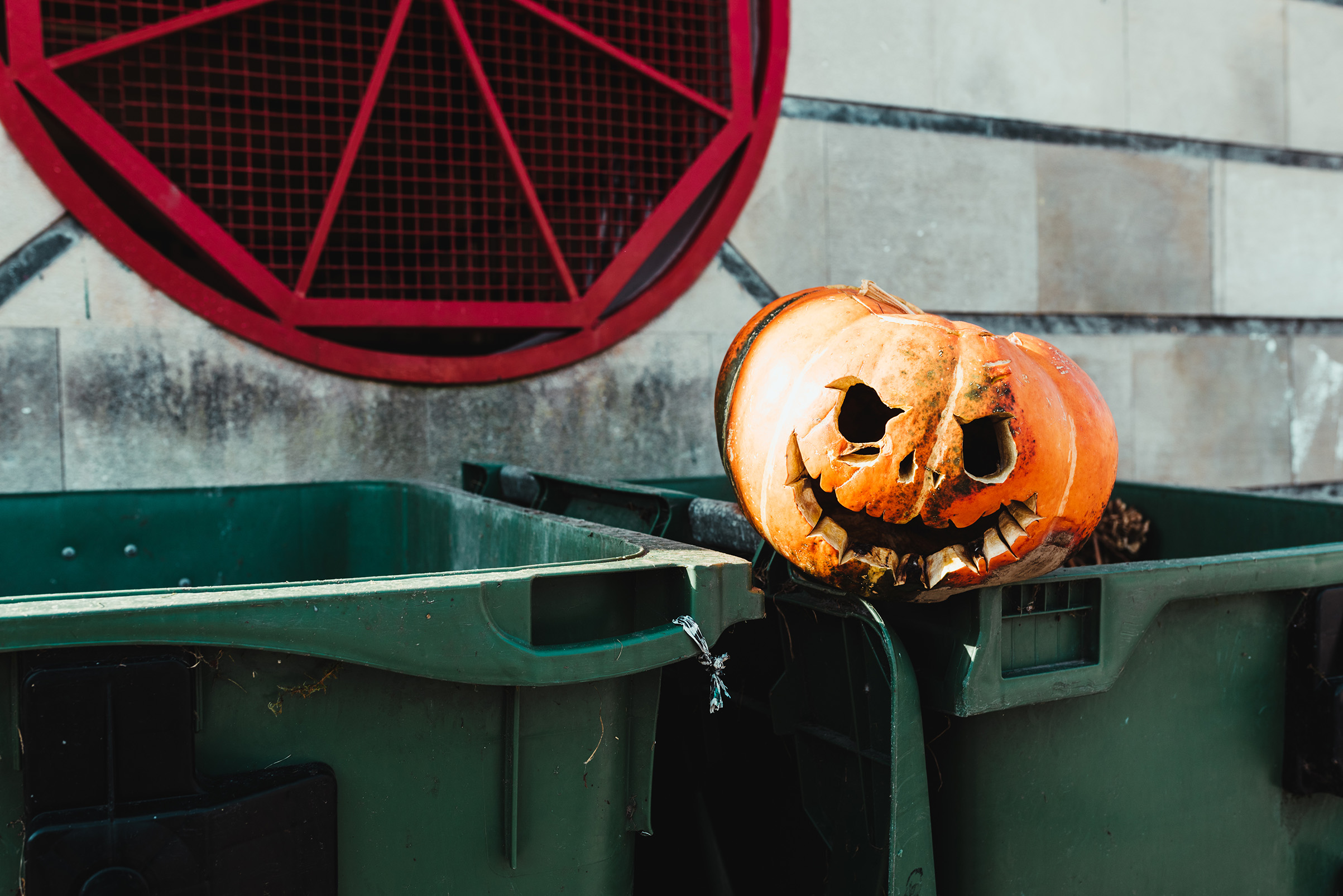 Halloween pumpkin with a carved and rotten face on top of some trash cans