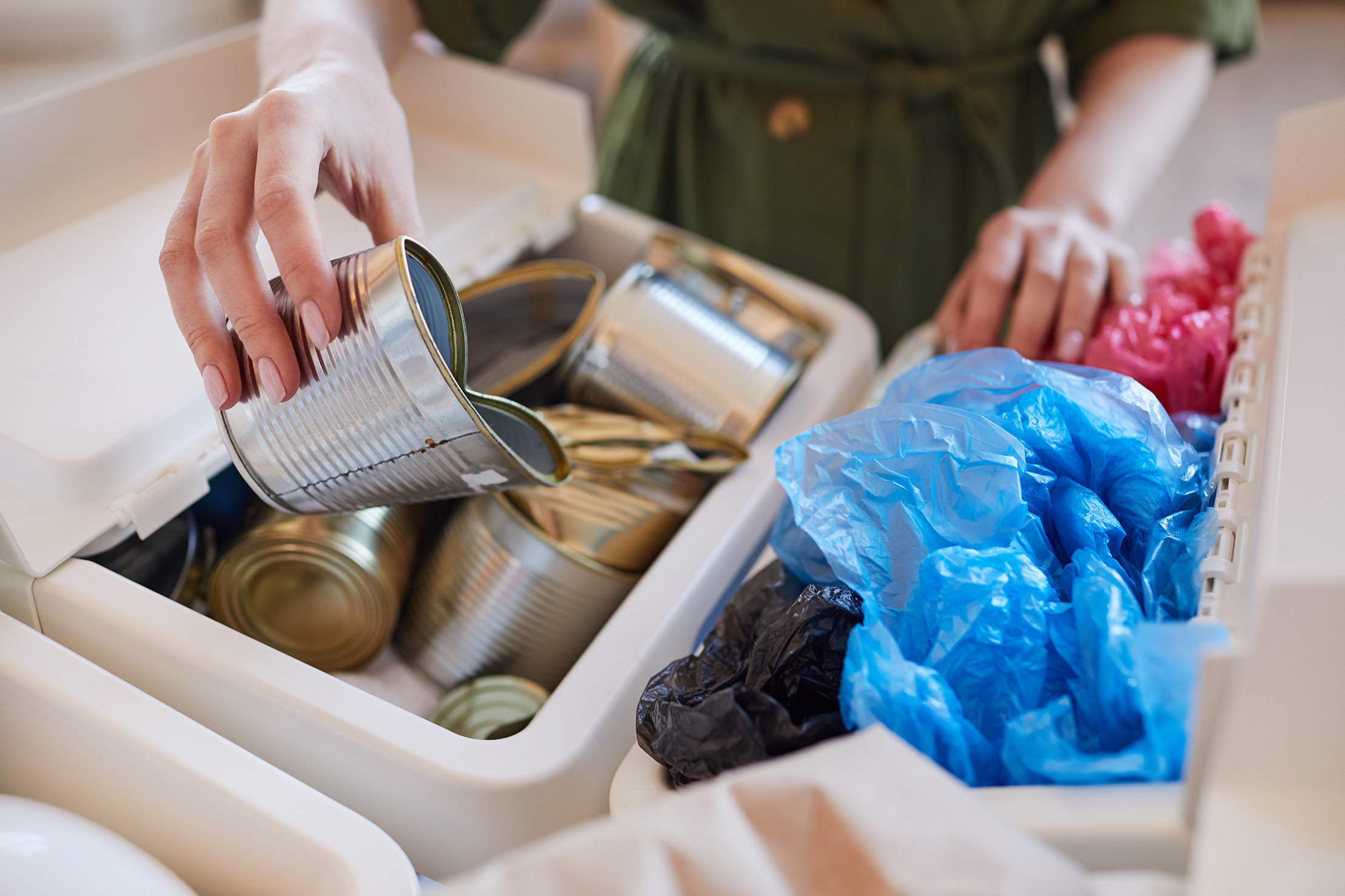 Close up of woman putting discarded metal cans into trash bin while sorting waste at home